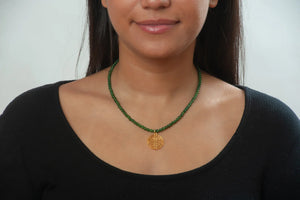 Image of girl in black top wearing gold Shou symbol pendant on necklace of green beads.