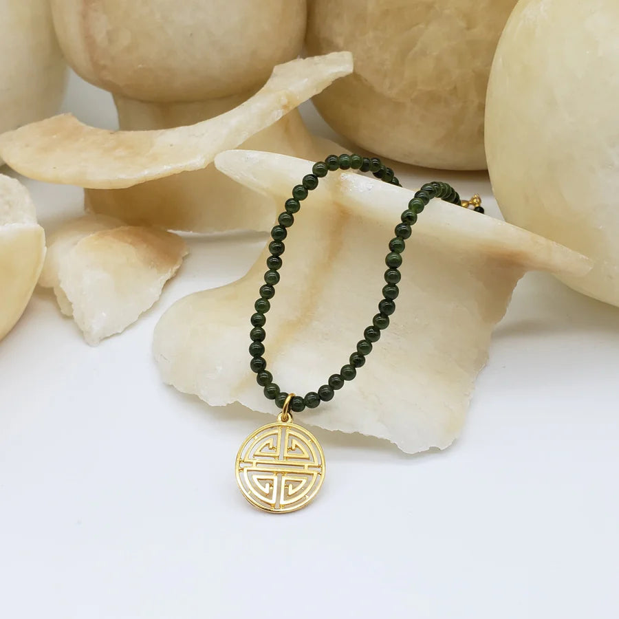 Image of gold Shou symbol pendant on necklace of green beads hanging on cream crystal.