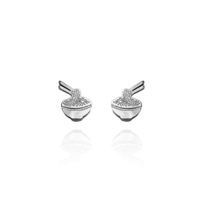 Pair of silver-tone stud earrings shaped like noodle bowls with chopsticks. The earrings feature intricate etched detailing representing noodles and utensils, with a reflective surface and a minimalist, playful design.