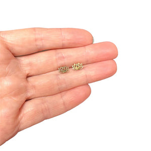 Image of a close-up of a hand holding a pair of gold-tone lotus flower shaped stud earrings, showcasing their small size and cut out details.