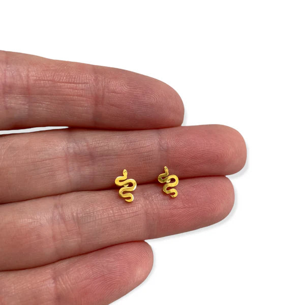 Image of a pair of small, gold-colored snake-shaped stud earrings displayed on the fingers of a person's hand, highlighting their petite size and coiled design.