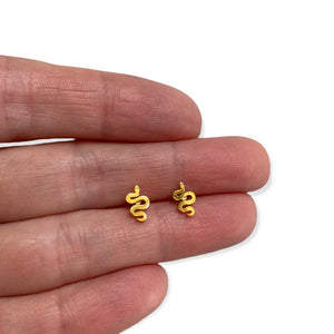Image of a pair of small, gold-colored snake-shaped stud earrings displayed on the fingers of a person's hand, highlighting their petite size and coiled design.