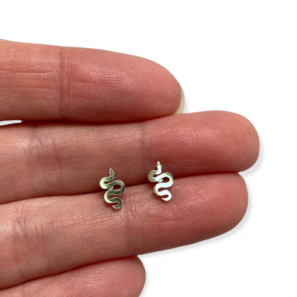 Image of a pair of small, silver-colored snake-shaped stud earrings displayed on the fingers of a person's hand, highlighting their petite size and coiled design.