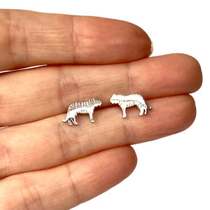 Image of a close-up of a hand holding a pair of silver-tone tiger-shaped stud earrings, showcasing their small size and engraved stripe details.