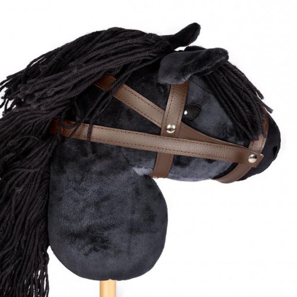Close up image of black hobbie horse, showing black plush horse head with black main and brown bridle attached to a pine stock, on white background.