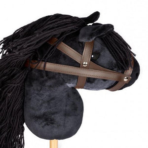 Close up image of black hobbie horse, showing black plush horse head with black main and brown bridle attached to a pine stock, on white background.