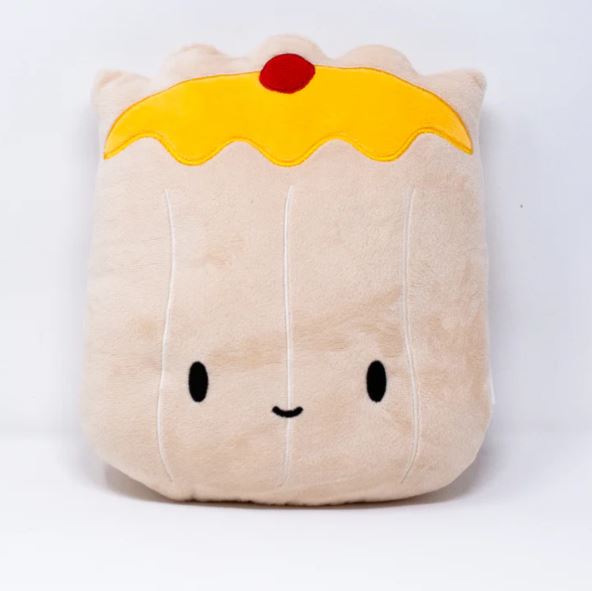 Front view image of a plush pillow shaped like a siu mai dumpling, featuring a light beige body with stitched vertical lines, a yellow “wrapper” top with a red dot resembling roe or garnish, and a cute embroidered face with black oval eyes and a small smiling mouth.