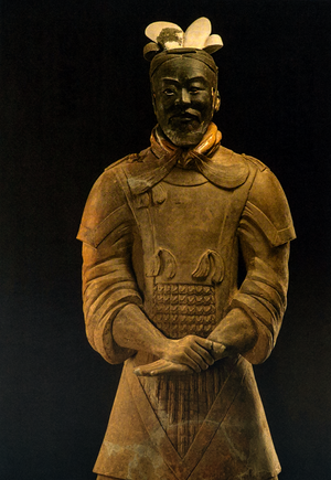 Postcard featuring a terracotta warrior statue in detailed armor with scaled chest plate and layered shoulder guards; set against a dark background.