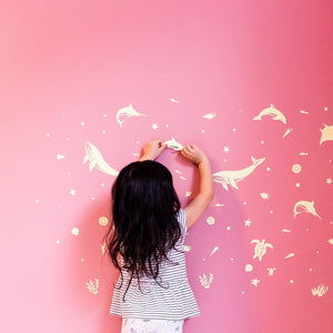 Girl sticking sea animal glow in the dark stickers on a pink wall.