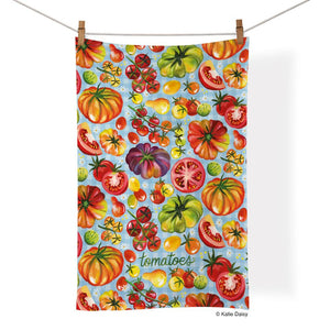 Tea towel with colourful illustrations of whole, sliced, and cherry tomatoes on a light blue background.